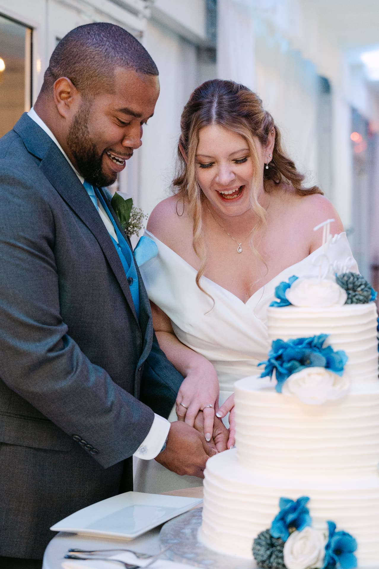 Newlyweds laughing while cutting their wedding cake at the reception