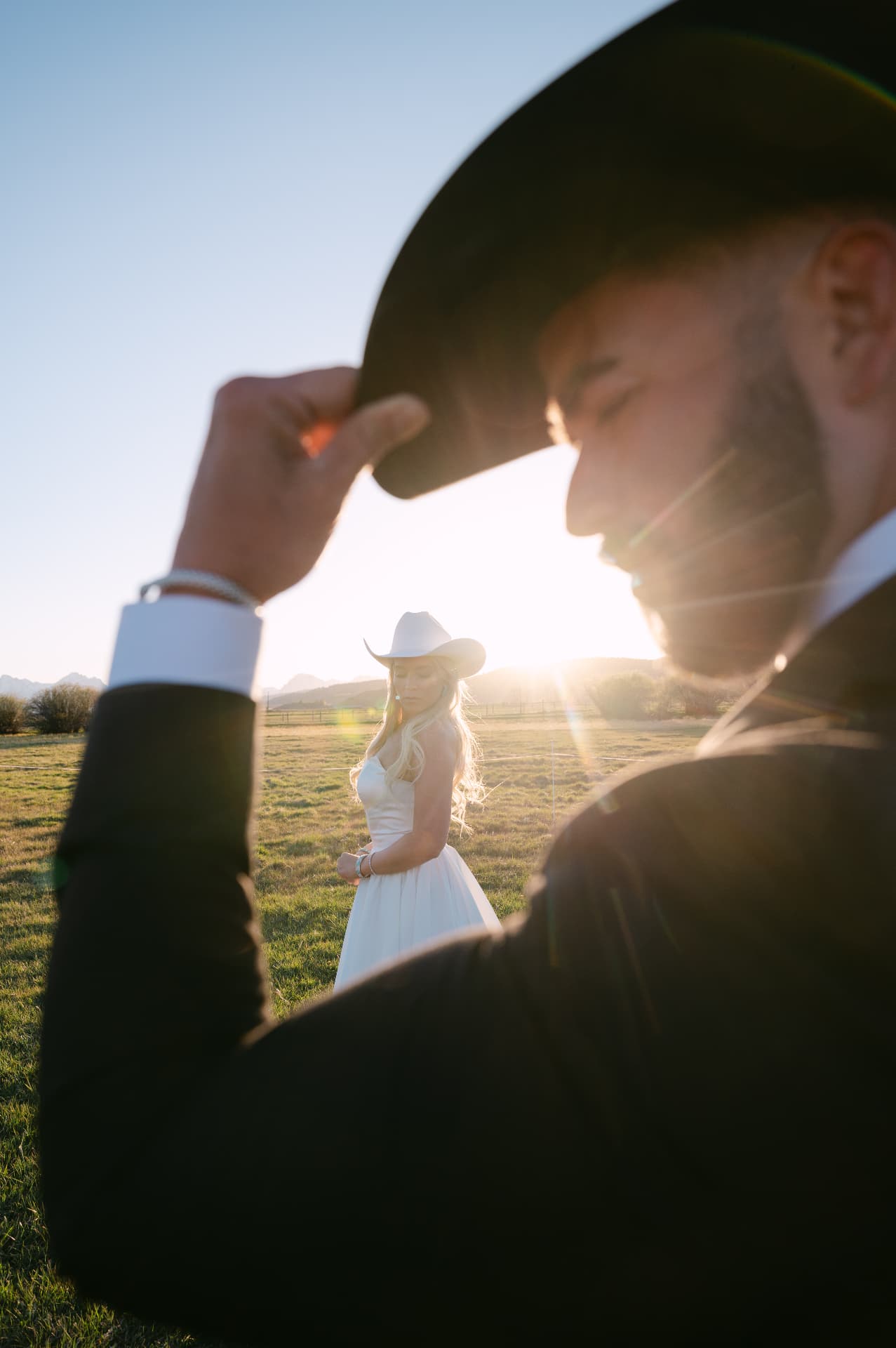 One partner tipping their hat toward the other in an open field at sunset