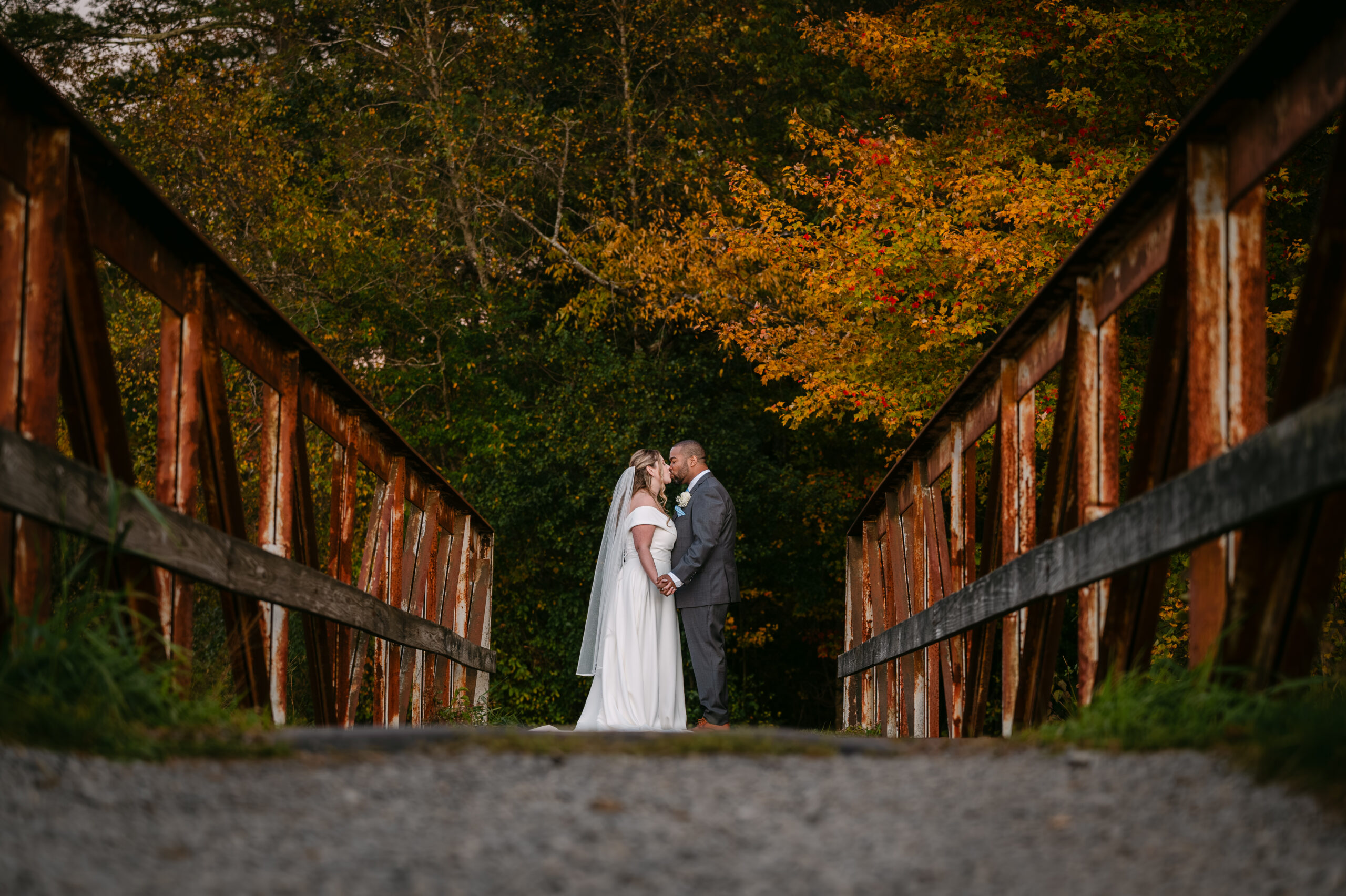 A bride and groom standing on a wooden bridge surrounded by vibrant fall foliage during their wedding at The Villa at Ridder Country Club in East Bridgewater, Massachusetts.