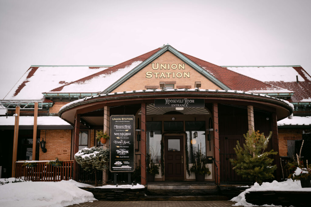 Exterior of Union Station Banquets in winter, featuring the historic train station architecture, snow-covered rooflines, and the Roosevelt Room entrance. Warm brick details and vintage signage create a timeless and elegant wedding venue atmosphere. Photographed by Massachusetts wedding Photographer