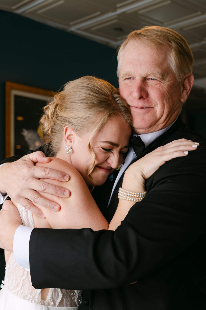  Massachusetts wedding Photographer captures Bride sharing an emotional embrace with her father during her wedding day at Union Station Banquets. The candid moment captures the bride smiling through tears while her father holds her close in a heartfelt and intimate portrait.