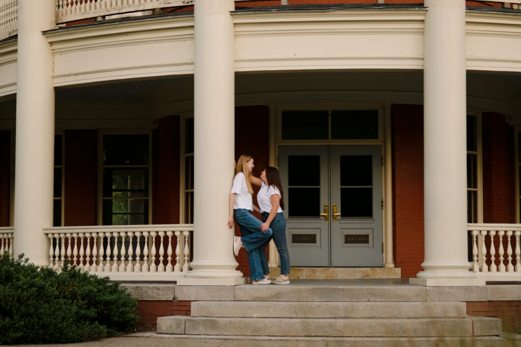 LGBTQ+ couple Jamielin and Sara posing on the grand columns of the Roger Williams Park Casino for their engagement photos.